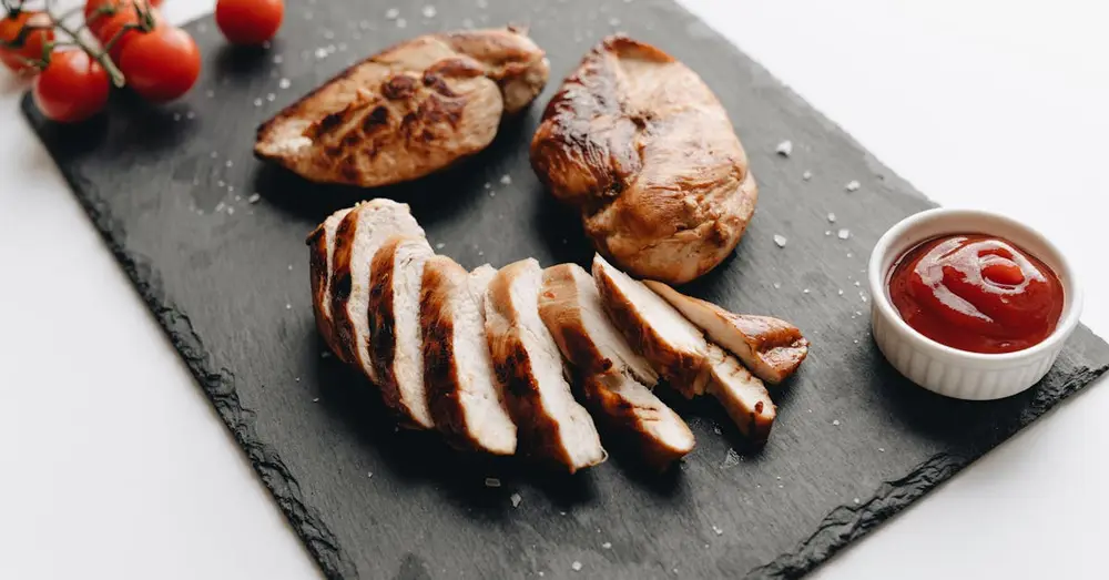Sliced grilled chicken breast on slate with cherry tomatoes and dipping sauce.