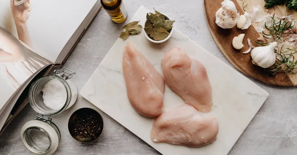 Flat lay of chicken breasts with ingredients for cooking, including garlic and olive oil.