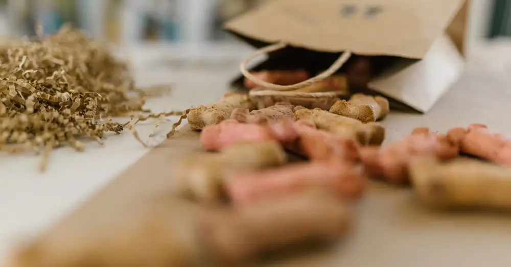 A paper bag spilling colorful dog treats amidst shredded confetti on a table.