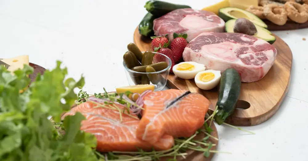 Assorted fresh keto ingredients including salmon, beef, and vegetables on wooden boards, perfect for healthy meals.