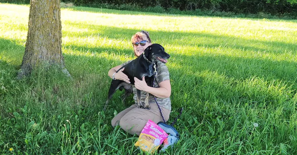Jodi hugs one of her dogs beside a bag of SitStay Chicken Chips