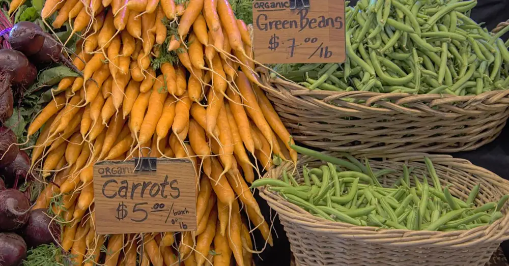 A display of fresh organic carrots and green beans at a local market stall.